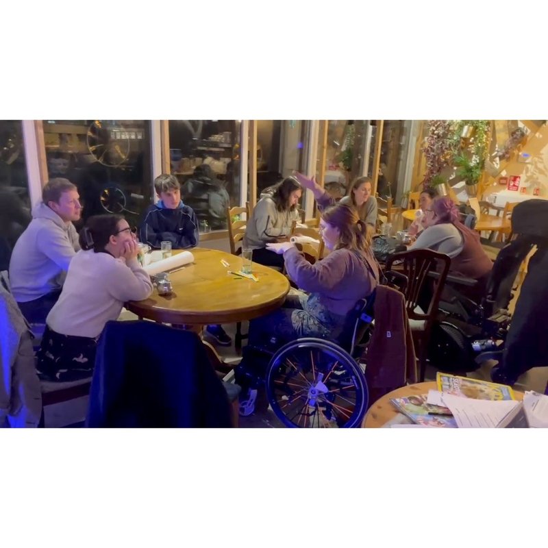 Two groups of people working together at tables, some of the people are in wheelchairs